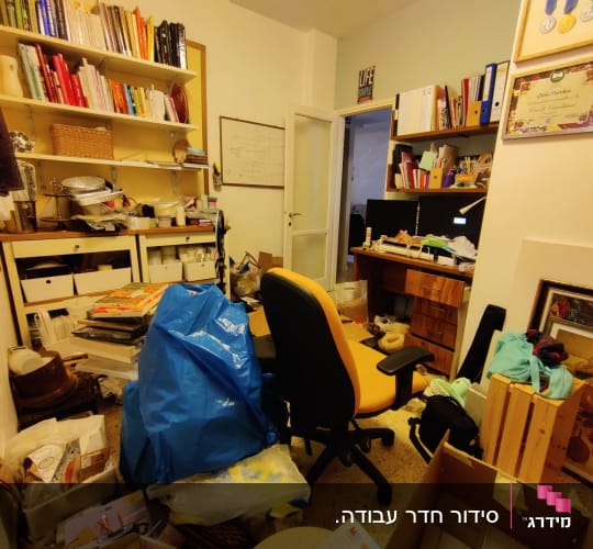 חדר מבולגן עם מדפים, כיסא ומחשב, חפצים מפוזרים